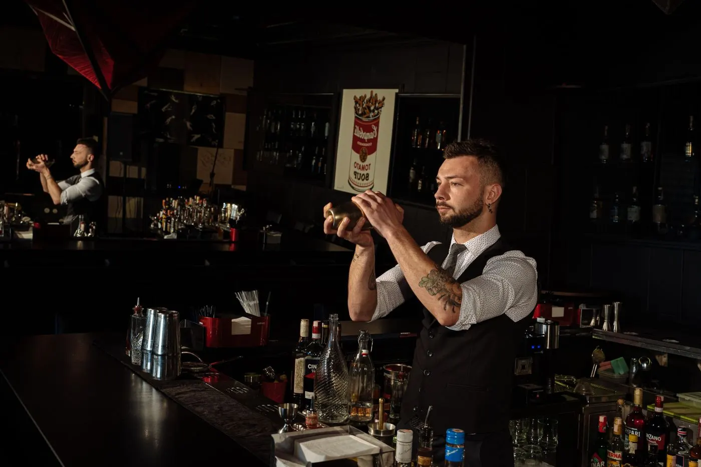 A bartender shaking a cocktail in a metal shaker behind a dark bar