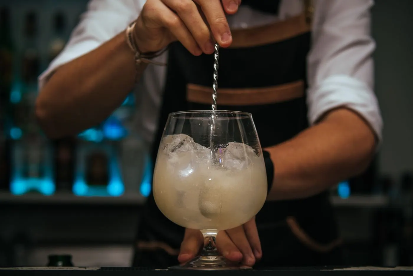 A bartender stirring a cocktail over ice in a stemmed glass with a long bar spoon